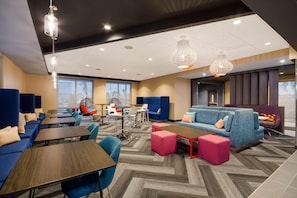 A modern hotel lobby with blue sofas, wooden tables, and a mix of seating options including chairs and ottomans. - Tru By Hilton Destin (Destin)