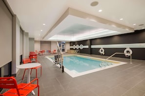 A swimming pool area with red chairs and tables, a lifeguard stand, and a dark wall with a white decorative element. - Tru By Hilton Destin (Destin)