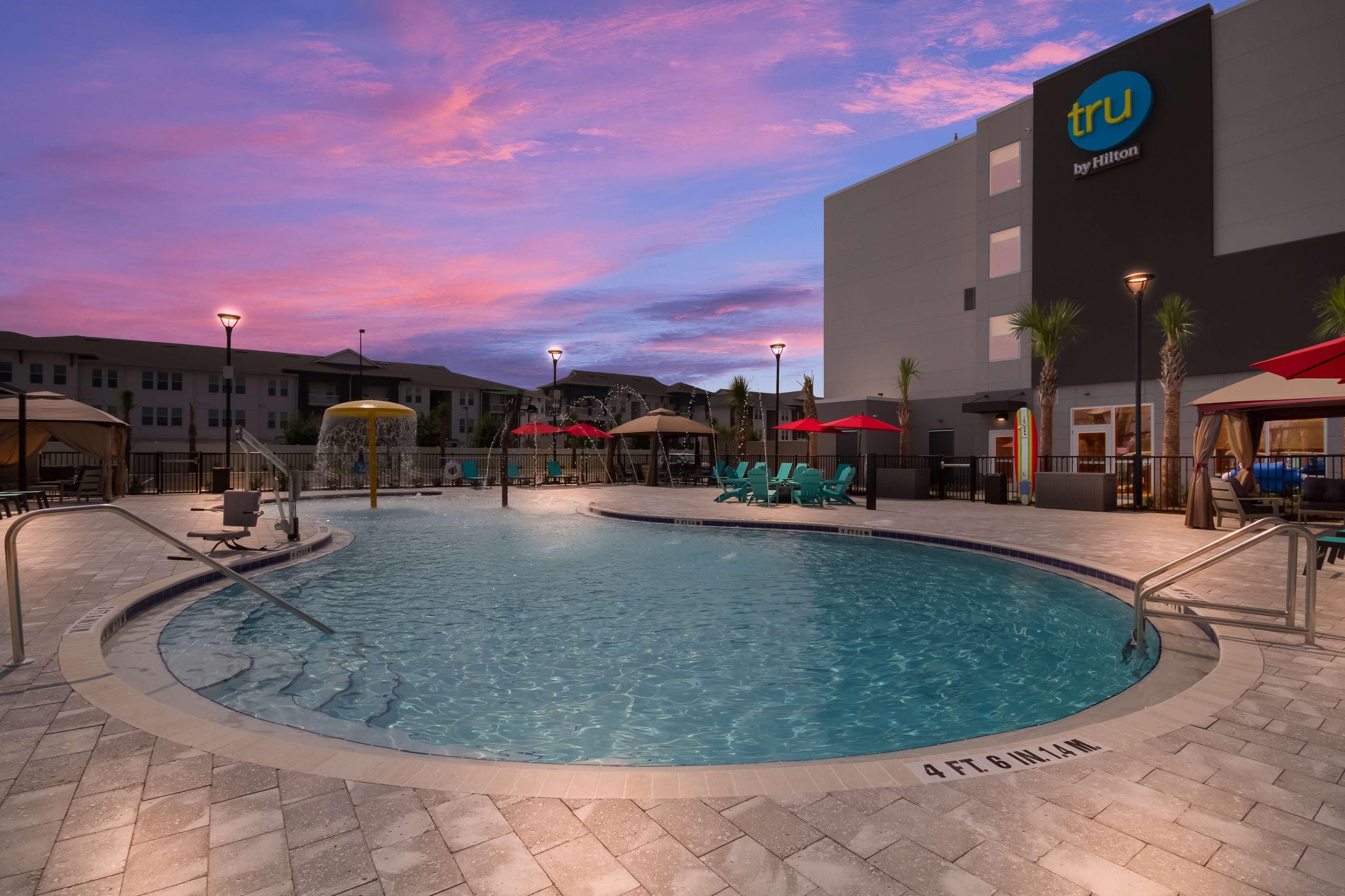 A swimming pool with a surrounding deck, lounge chairs, and umbrellas.