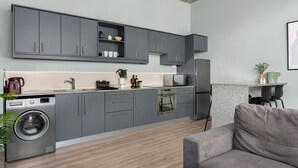 Una cocina moderna con armarios grises, lavadora integrada y un comedor con sofá gris.