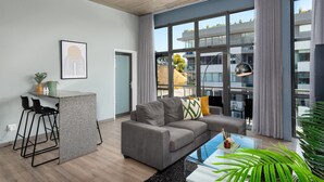 Una sala de estar moderna con un sofá gris, una pequeña zona de bar y amplias ventanas con vistas a la ciudad.