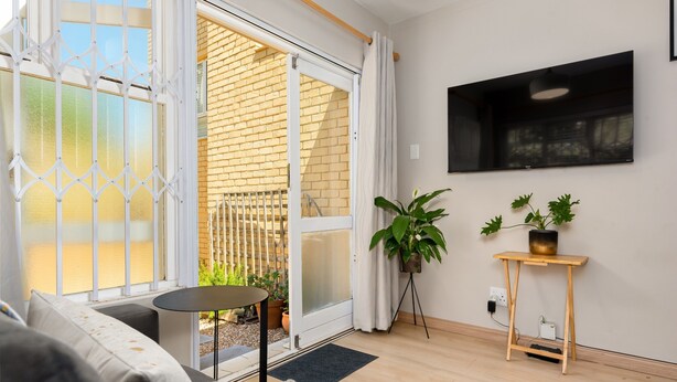 Een moderne woonkamer met een bank, een bijzettafeltje, een potplant en een aan de muur bevestigde televisie.