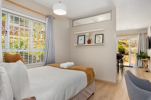 Un dormitorio moderno con una cama grande, un escritorio pequeño, una silla y un balcón con plantas.