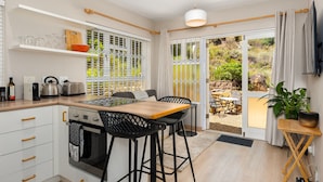 Een moderne keuken met een houten aanrecht, witte kastjes en een ingebouwde oven. Er is een eethoek met een tafel en stoelen, en een schuifdeur die leidt naar een terras.