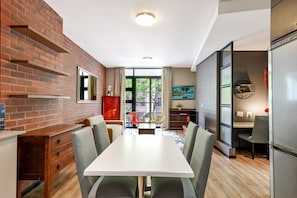 Une cuisine moderne avec un mur en briques, un coin repas avec une table blanche et un réfrigérateur.