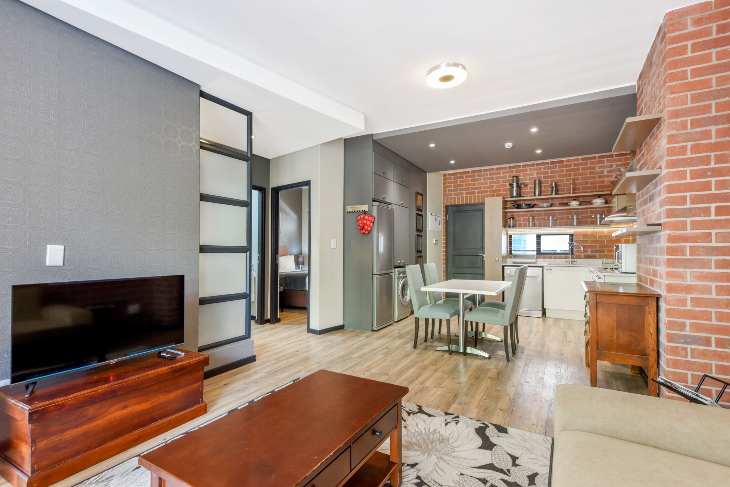 A modern living room with a flat-screen TV, wooden furniture, and a dining area with a table and chairs.
