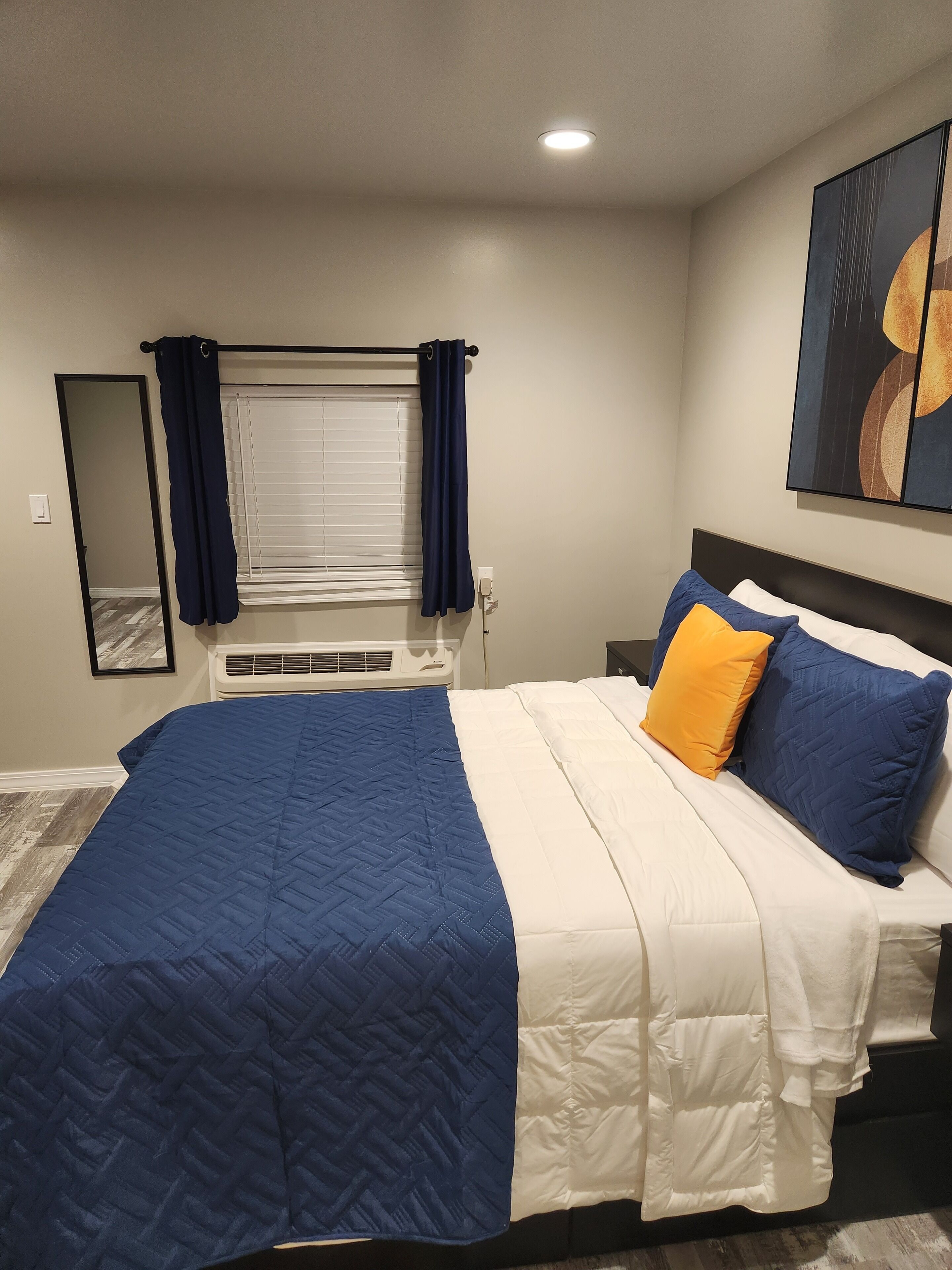 Quarto com cama, janela com cortinas, aparelho de ar condicionado e um quadro na parede.