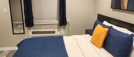 Quarto com cama, janela com cortinas, aparelho de ar condicionado e um quadro na parede.