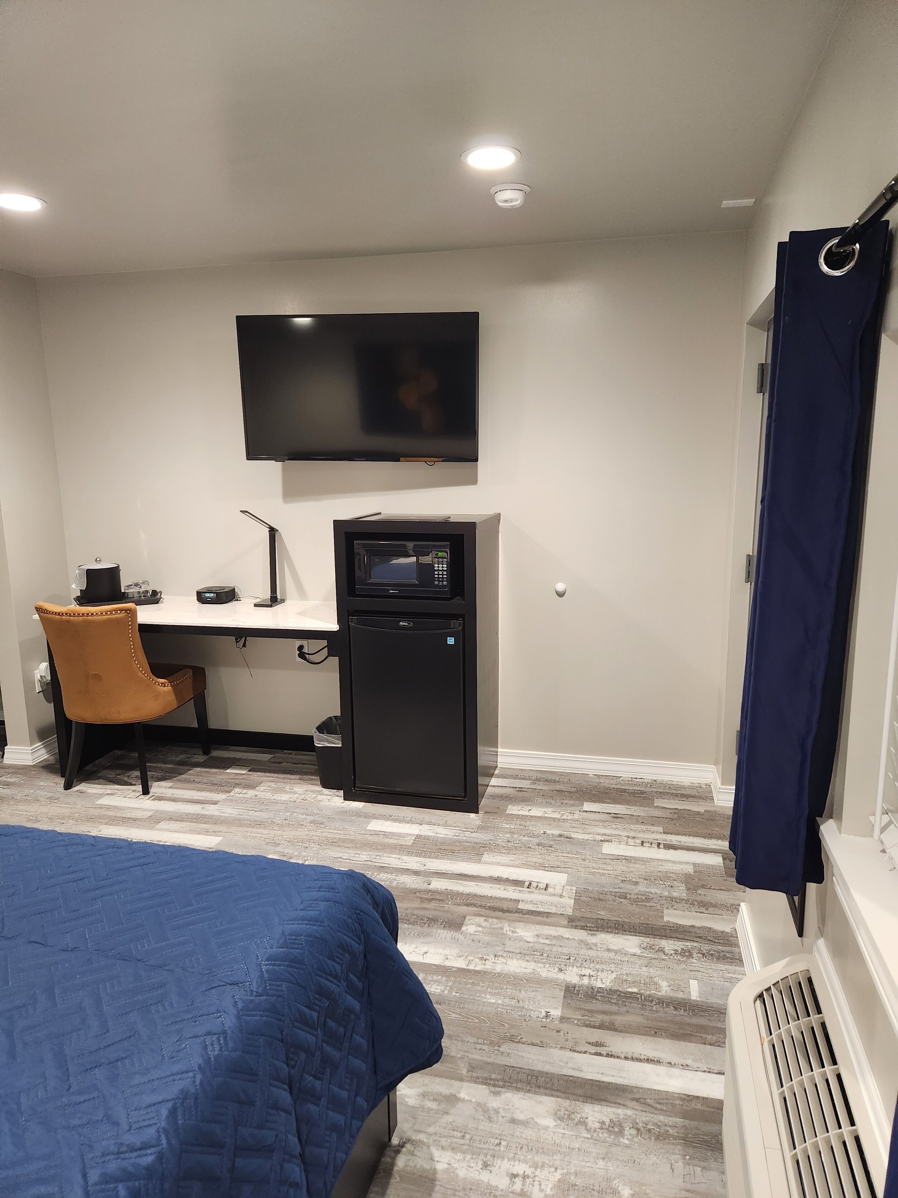 Una habitación de hotel con una cama, un escritorio con una computadora, un microondas, un televisor y una ventana con cortinas.