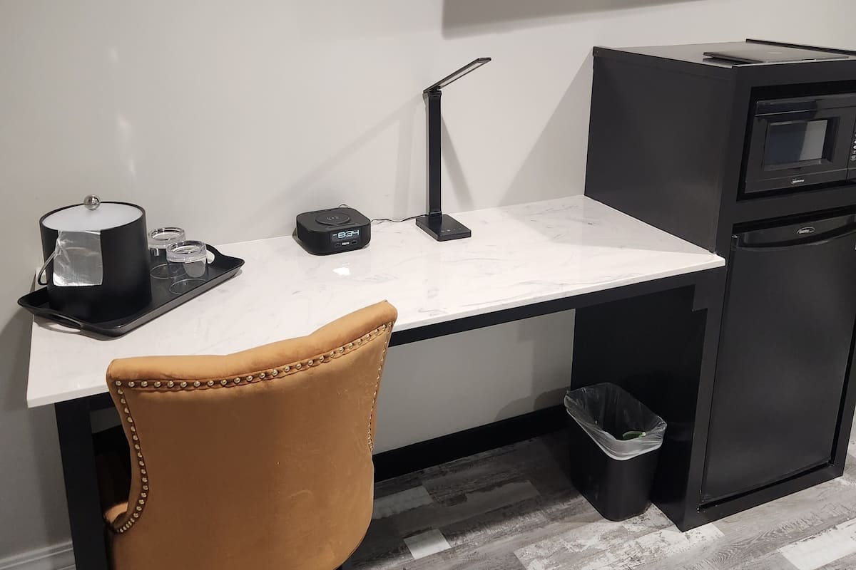 Uma cozinha moderna com bancada branca, geladeira preta, micro-ondas e cafeteira.