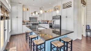 A spacious kitchen with white cabinetry, a central island with bar stools, and a stainless steel refrigerator. - A Wave From It All - Beautiful house, close to the beach with great views! (Crystal Beach)