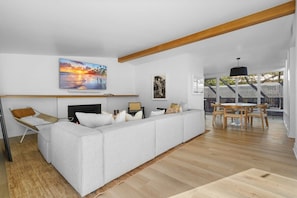 A modern living room with a sofa, a fireplace, and a dining area with a table and chairs. - Malibu Beach House by Stay Awhile Villas (Malibu)