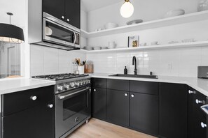 A modern kitchen with black cabinets, white countertops, a built-in oven, a microwave, and a hanging light fixture.