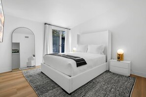 A modern bedroom with a large bed, bedside tables, a mirror, and a window with curtains.