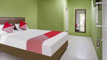 A hotel room with a bed, green walls, a mirror, and a door.