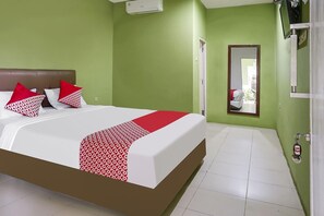 A hotel room with a bed, green walls, a mirror, and a door.