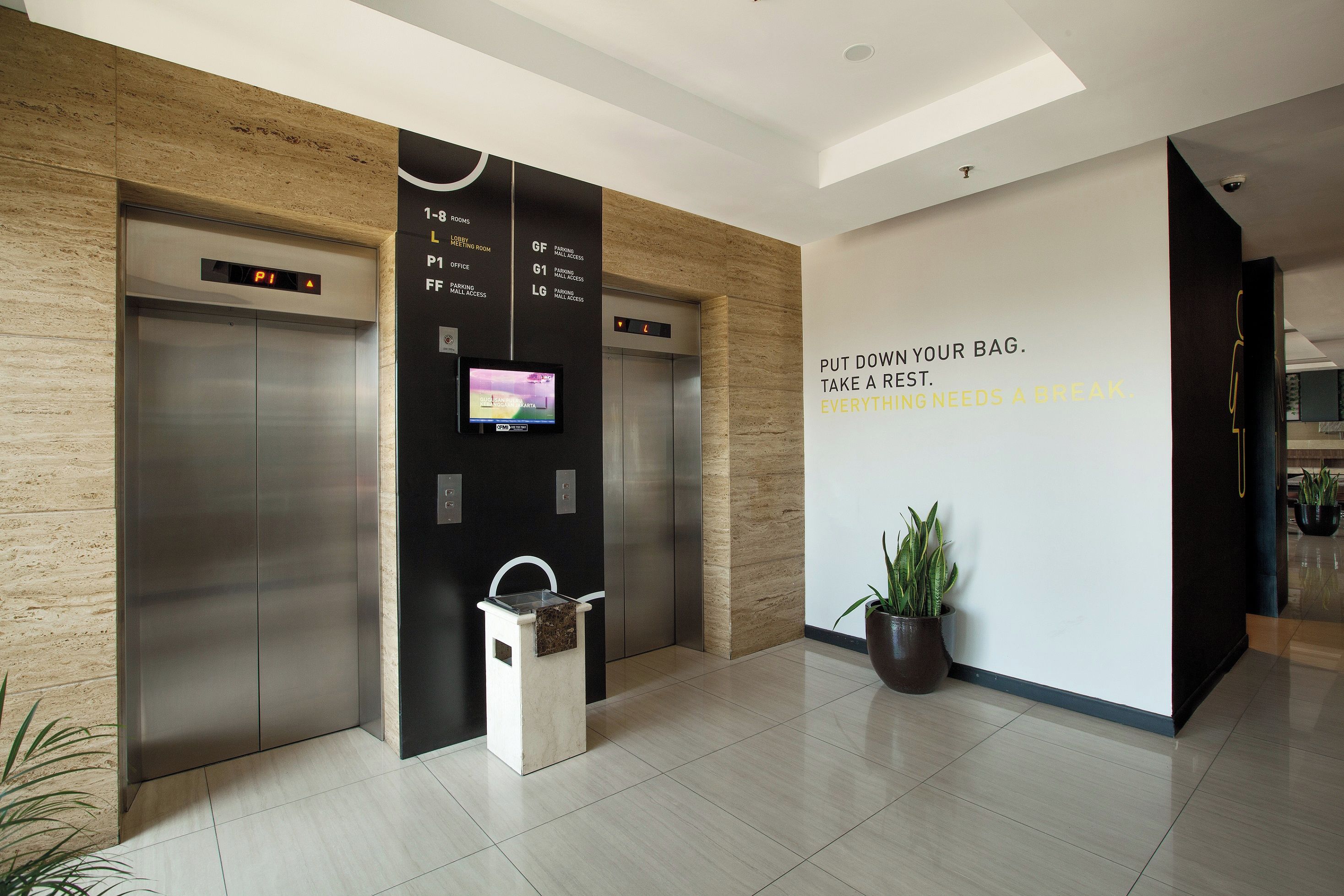 A modern elevator with digital displays, a wall-mounted television, and a motivational quote.