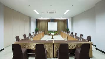 Uma sala de conferências com uma mesa comprida, cadeiras, uma tela de projetor e uma planta.