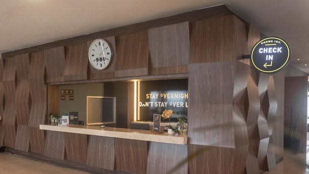 A reception desk with a clock, a sign that says "CHECK IN," and a message encouraging guests not to stay over night. - Rooms Inc BTC Pasteur (Bandung)