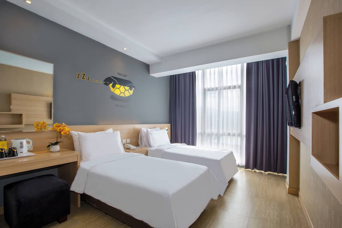 A hotel room with two beds, a desk with a coffee maker, a TV, and a large window with curtains.