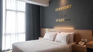 A hotel room with a bed, a bedside table with a phone, and a wall with motivational text. - Rooms Inc BTC Pasteur (Bandung)