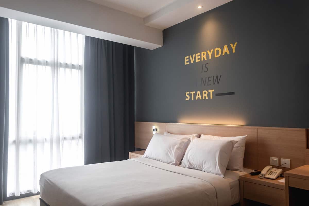A hotel room with a bed, a bedside table with a phone, and a wall with motivational text.