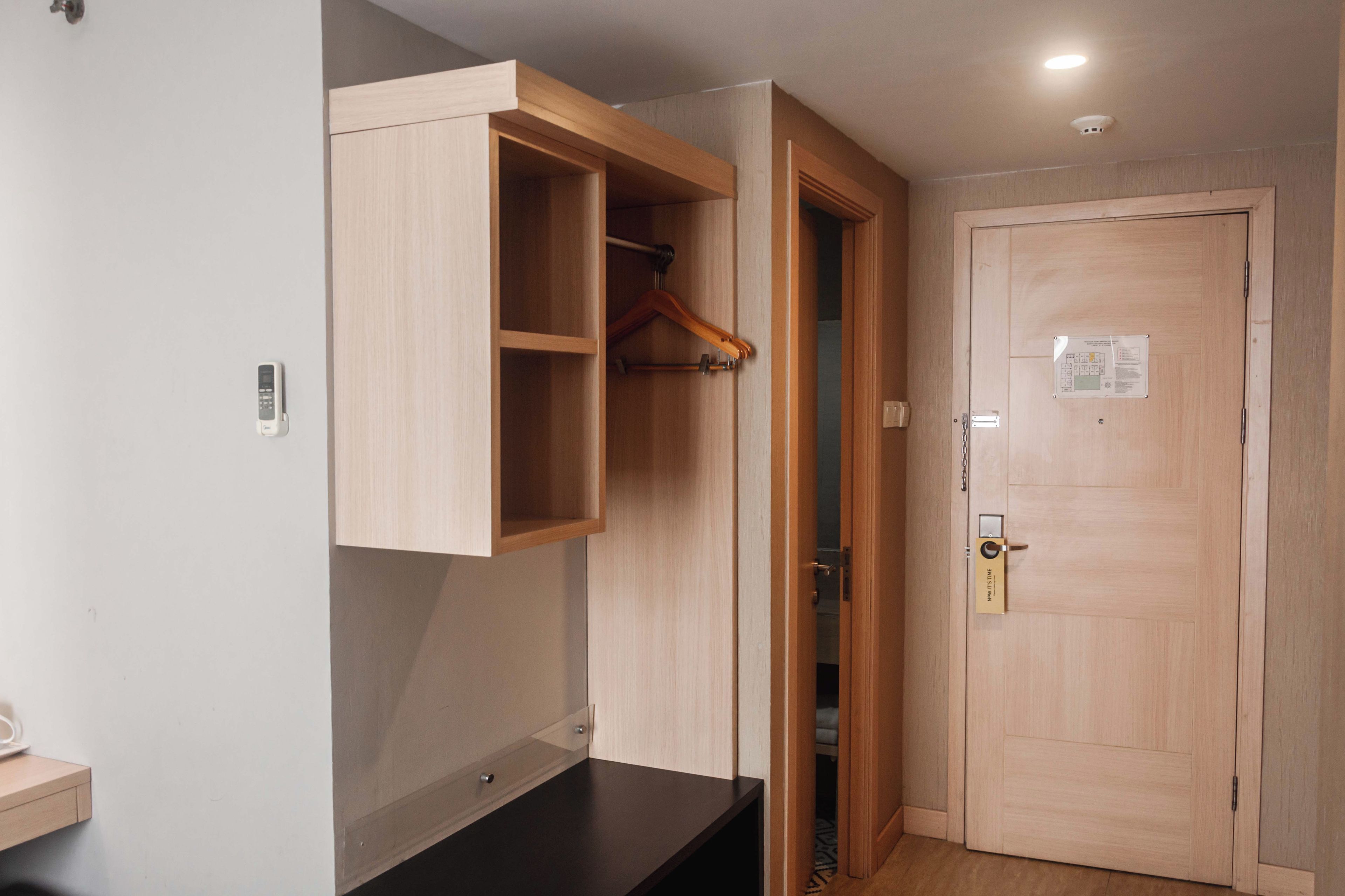 Ein Zimmer mit einem Holzschrank, einer verschließbaren Tür und einem kleinen Regal mit einer Fernbedienung.