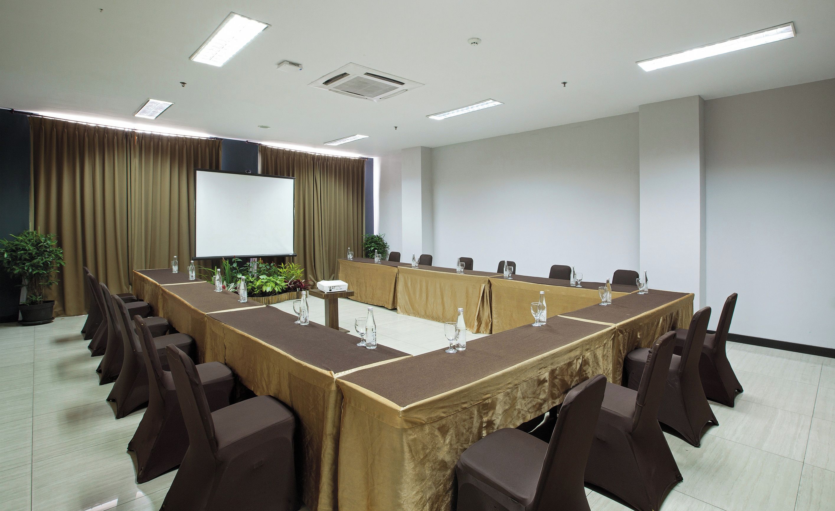 Ein Konferenzraum mit langem Tisch, Stühlen, einer Projektionsleinwand und einem Blumentopf.
