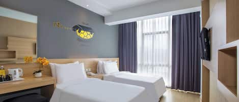 Quarto de hotel com duas camas, uma escrivaninha com cafeteira, televisão e uma janela grande com cortinas.