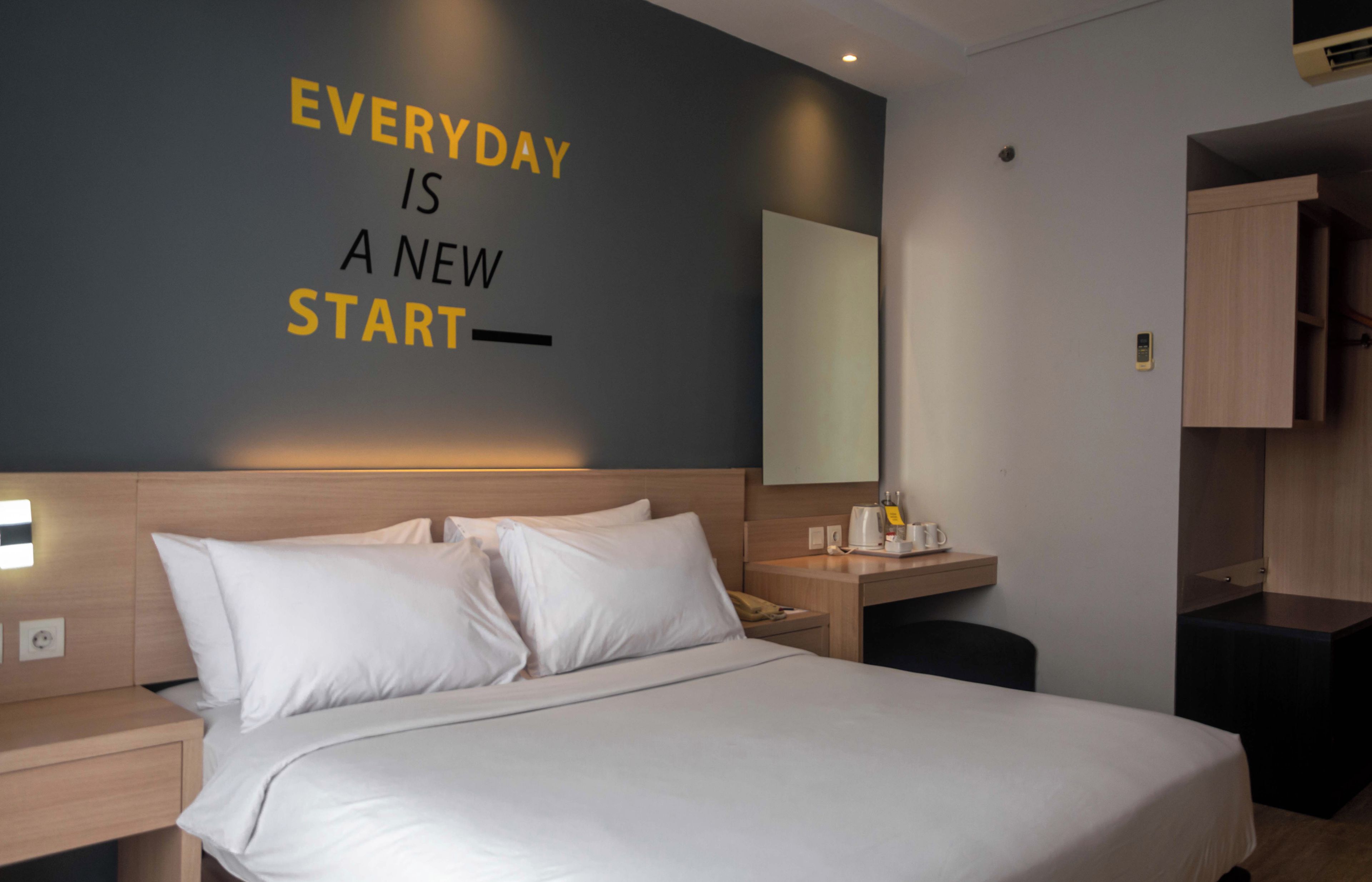 A hotel room with a bed, a bedside table, a nightstand, a mirror, and a wall with motivational text.