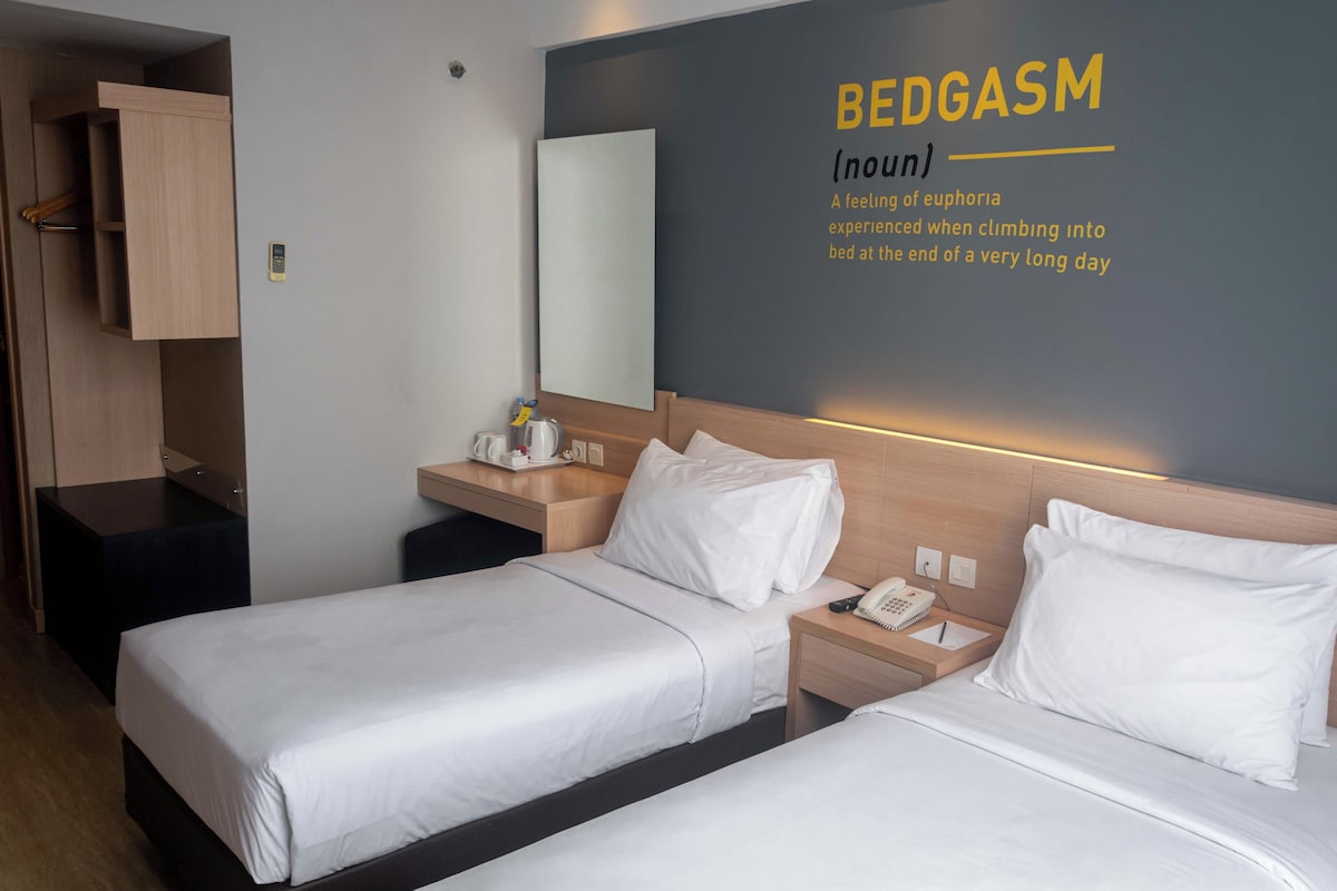 Ein Hotelzimmer mit zwei Betten, einem Nachttisch mit Telefon, einem kleinen Tisch mit Kaffeemaschine und einem Kleiderschrank.