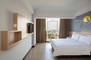 A hotel room with a large bed, a mounted TV, a wooden shelf, and a view of the city through the window. - Rooms Inc BTC Pasteur (Bandung)