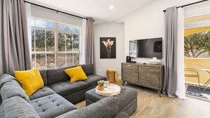 A modern living room with a grey sectional sofa, a round coffee table, and a flat-screen TV.