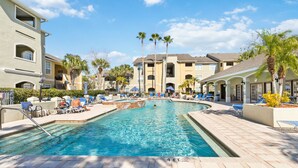 A swimming pool surrounded by lounge chairs and palm trees, with a clear sky above.
