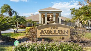 A sign for The Avalon with a number 1220 above it, surrounded by greenery and palm trees.