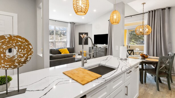 A modern kitchen with a marble countertop, wooden cutting board, and pendant lights.