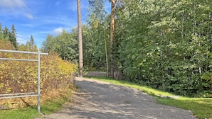 A gravel path leading through a wooded area with a metal gate on the left. - Muurame-City Studios (Muurame)