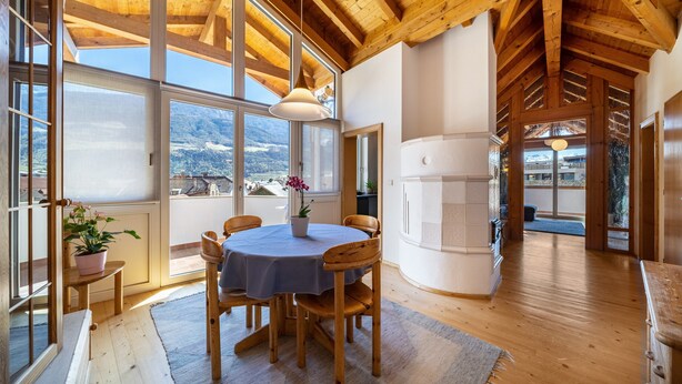 A wooden interior with a dining table, chairs, and a view through large windows. - Holiday Apartment "Luisa" with Mountain View, Private Terrace & Wi-Fi (Schlanders)