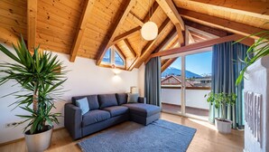 A modern living room with a wooden ceiling, a gray sectional sofa, a large potted plant, and a view of mountains through a sliding glass door. - Holiday Apartment "Luisa" with Mountain View, Private Terrace & Wi-Fi (Schlanders)
