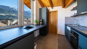 A modern kitchen with a wooden ceiling, a window with a view of mountains, and a built-in oven. - Holiday Apartment "Luisa" with Mountain View, Private Terrace & Wi-Fi (Schlanders)