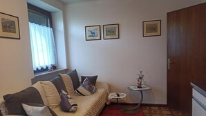 Una stanza con un divano, un tavolino, una finestra con tende e quadri appesi al muro.