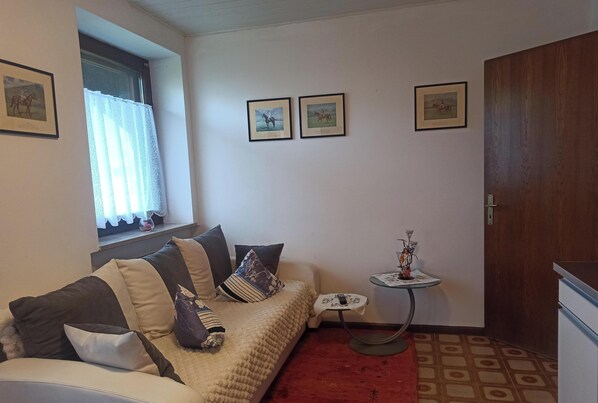A room with a sofa, a small table, a window with curtains, and framed pictures on the wall. - Apartment 'Jörg' with Large Shared Garden, Wi-Fi, and Optional Private Pool Use (Lana)