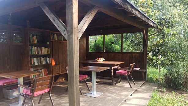 Una struttura in legno con tavolo e sedie, una libreria e una finestra che si affaccia sul verde.