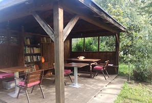 A wooden structure with a table and chairs, a bookshelf, and a window overlooking greenery.