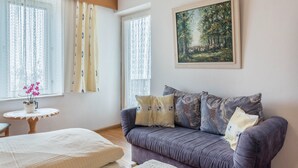 A room with a sofa, a small table with a plant, a painting on the wall, and a window with curtains. - Apartment 'Adang Ferienwohnung Fernblick' with Mountain View, Shared Garden and Wi-Fi (Tirolo)
