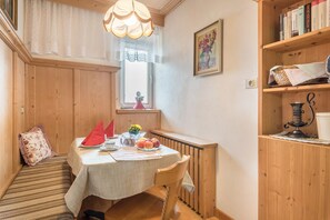 Un coin repas chaleureux avec une table dressée pour deux personnes, un banc en bois, une bibliothèque et une fenêtre ornée de rideaux en dentelle.
