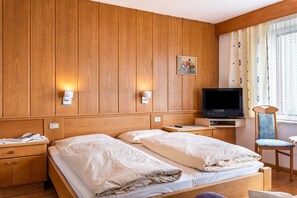 Une chambre d’hôtel avec des murs lambrissés, une télévision, deux lits, une chaise et une table de chevet avec un téléphone.