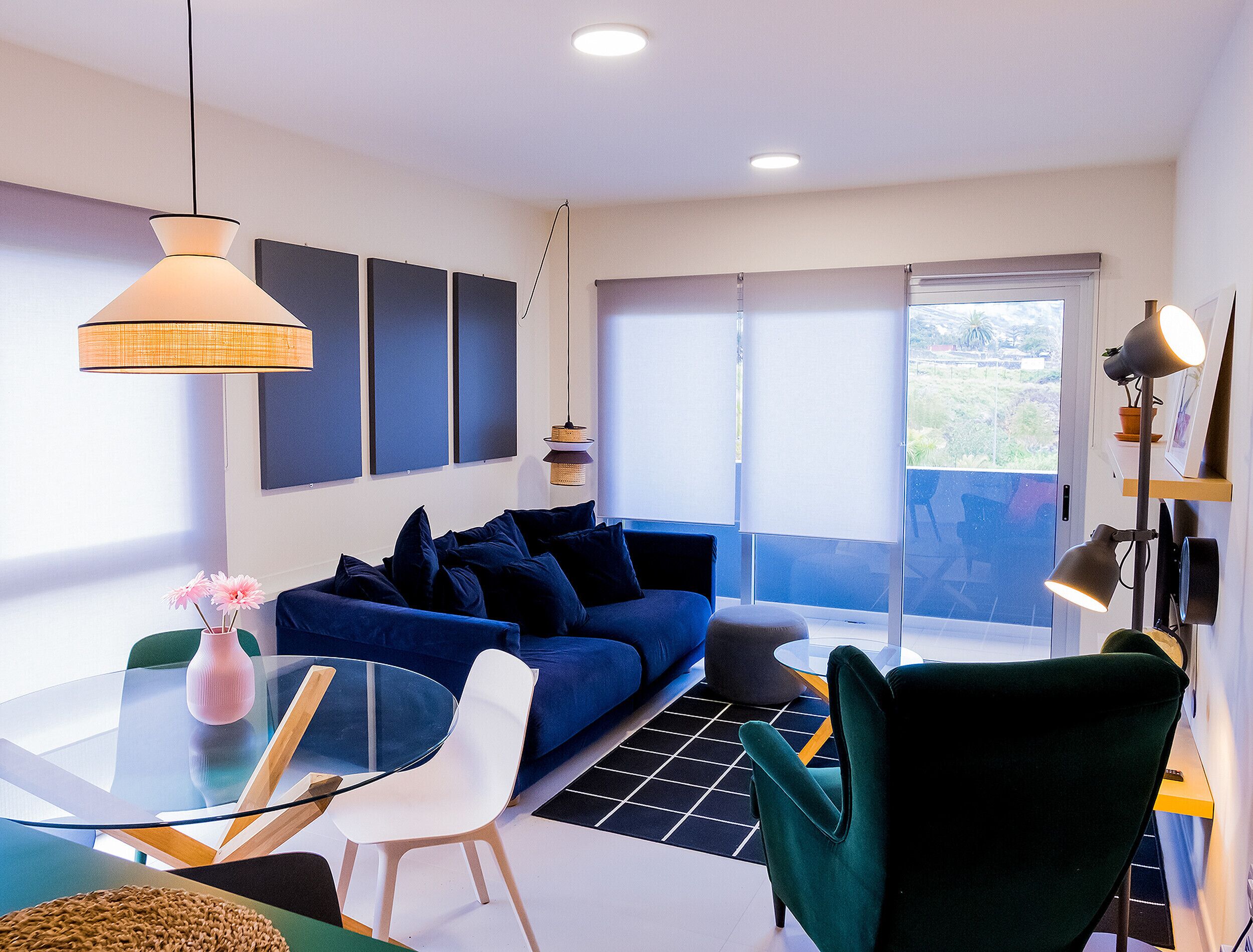 Een moderne woonkamer met een blauwe bank, een glazen salontafel en een groene fauteuil.