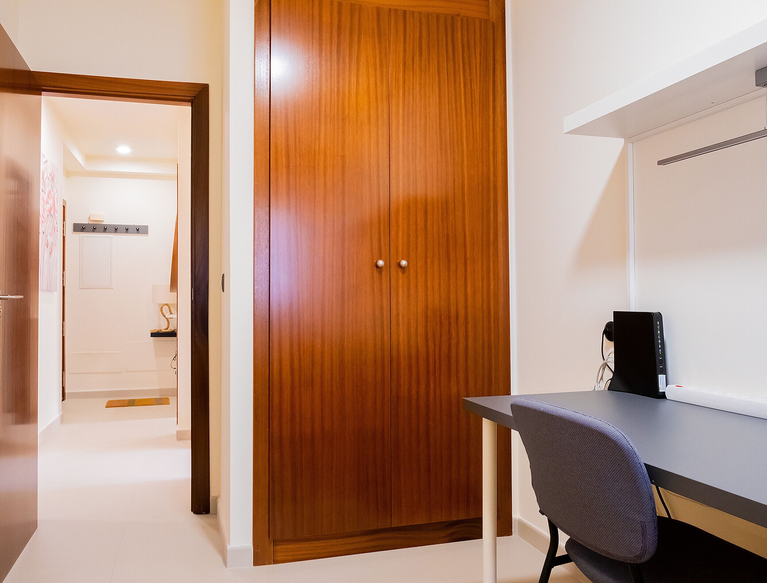 A room with a wooden wardrobe, a desk, and a chair.