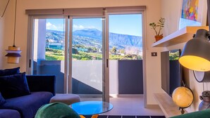 Una sala de estar moderna con un sofá, una mesa de vidrio y vistas a un paisaje montañoso a través de grandes puertas correderas.